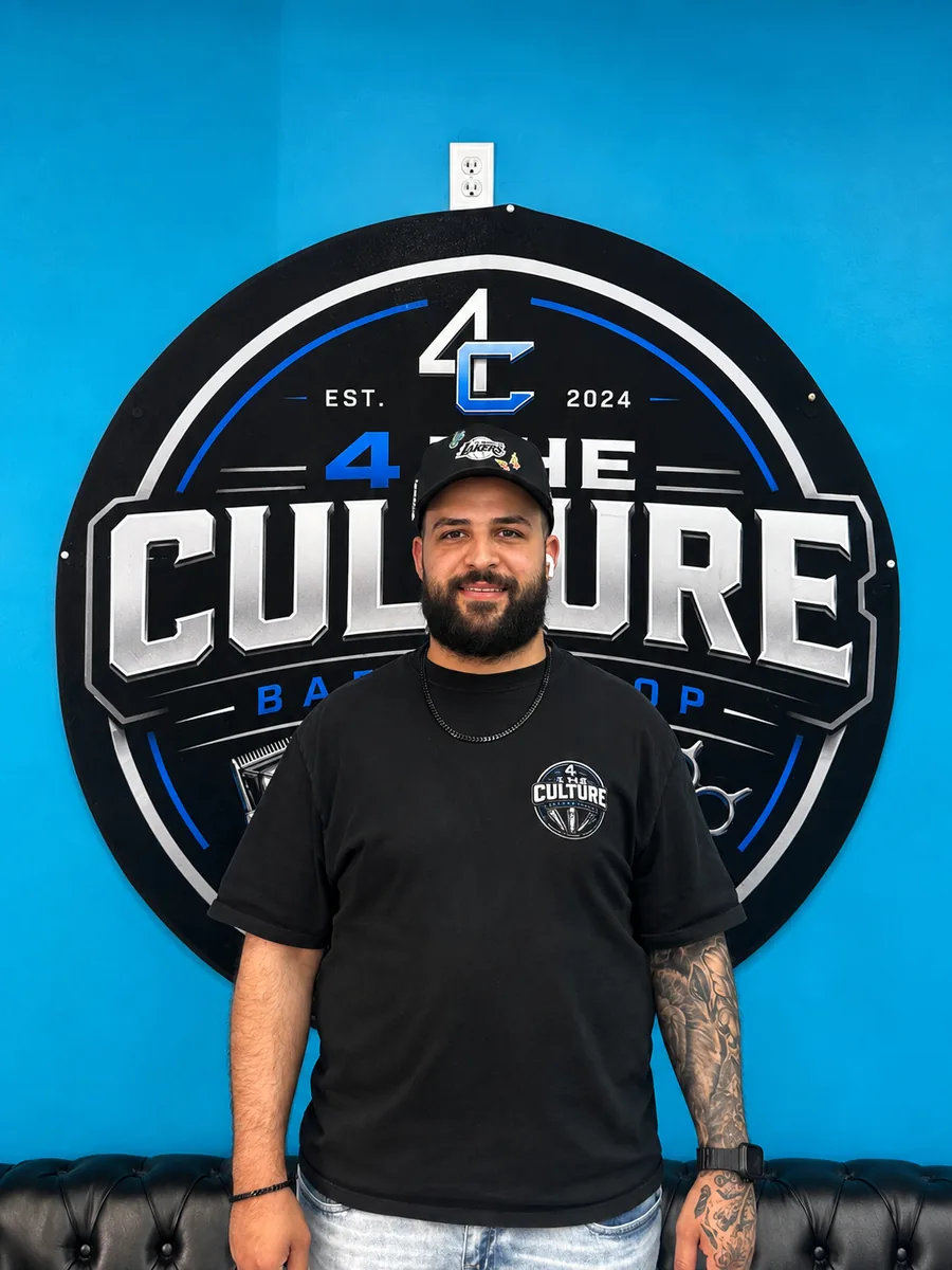 Ali, barber at 4 The Culture Barbershop, in front of the shop mural