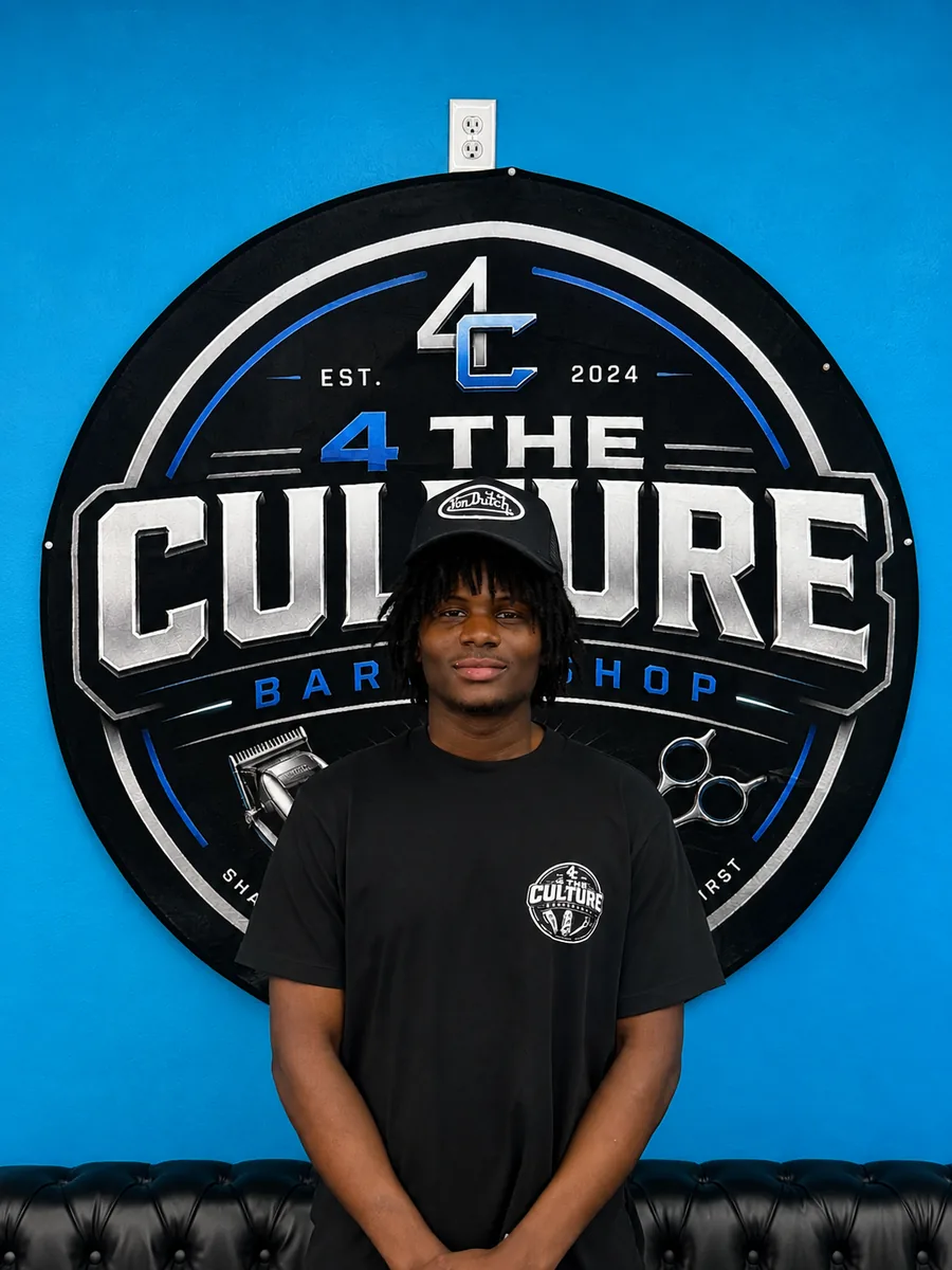Barber at chair 02 of 4 The Culture Barbershop, standing in front of the shop mural