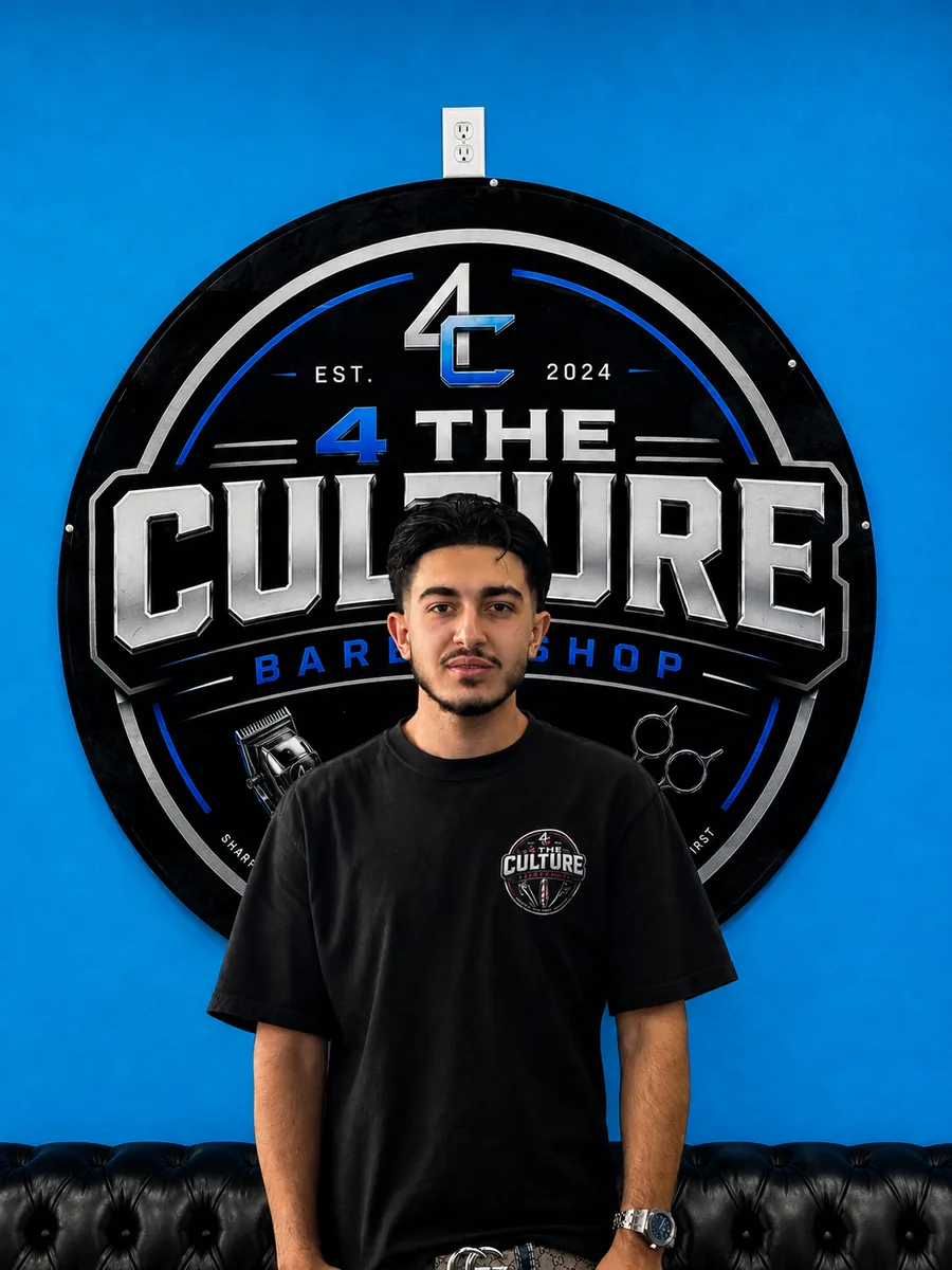 Rav, barber at 4 The Culture Barbershop, in front of the shop mural