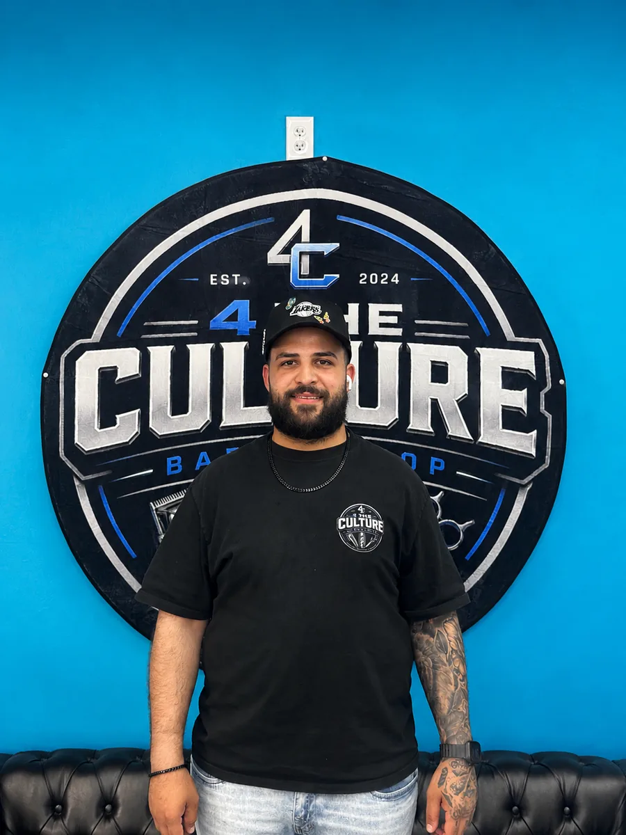 Barber at chair 04 of 4 The Culture Barbershop, standing in front of the shop mural